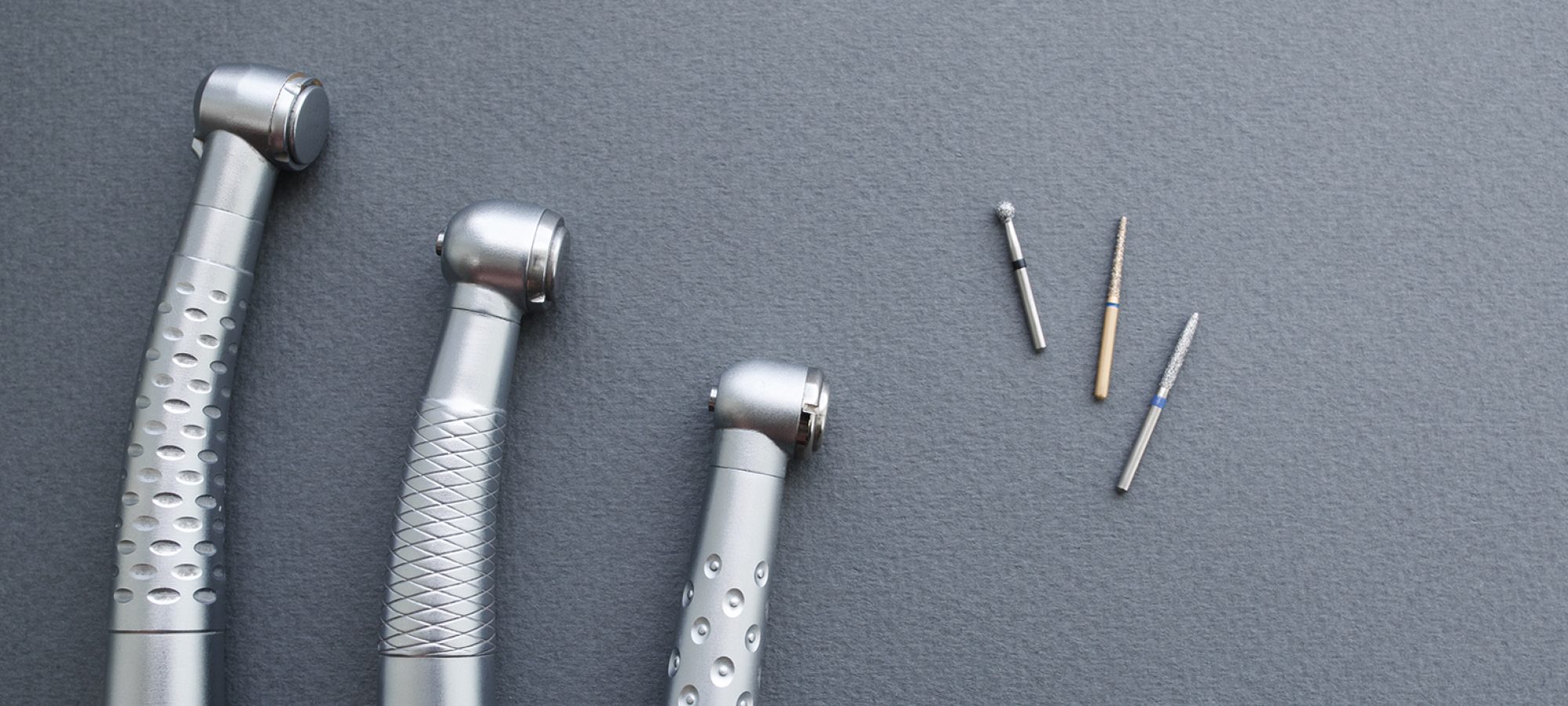 Dental turbine handpieces and burs apart free space. Dental equipment on gray background flat lay. Closeup of line of dental turbine handpieces with dental drills apart